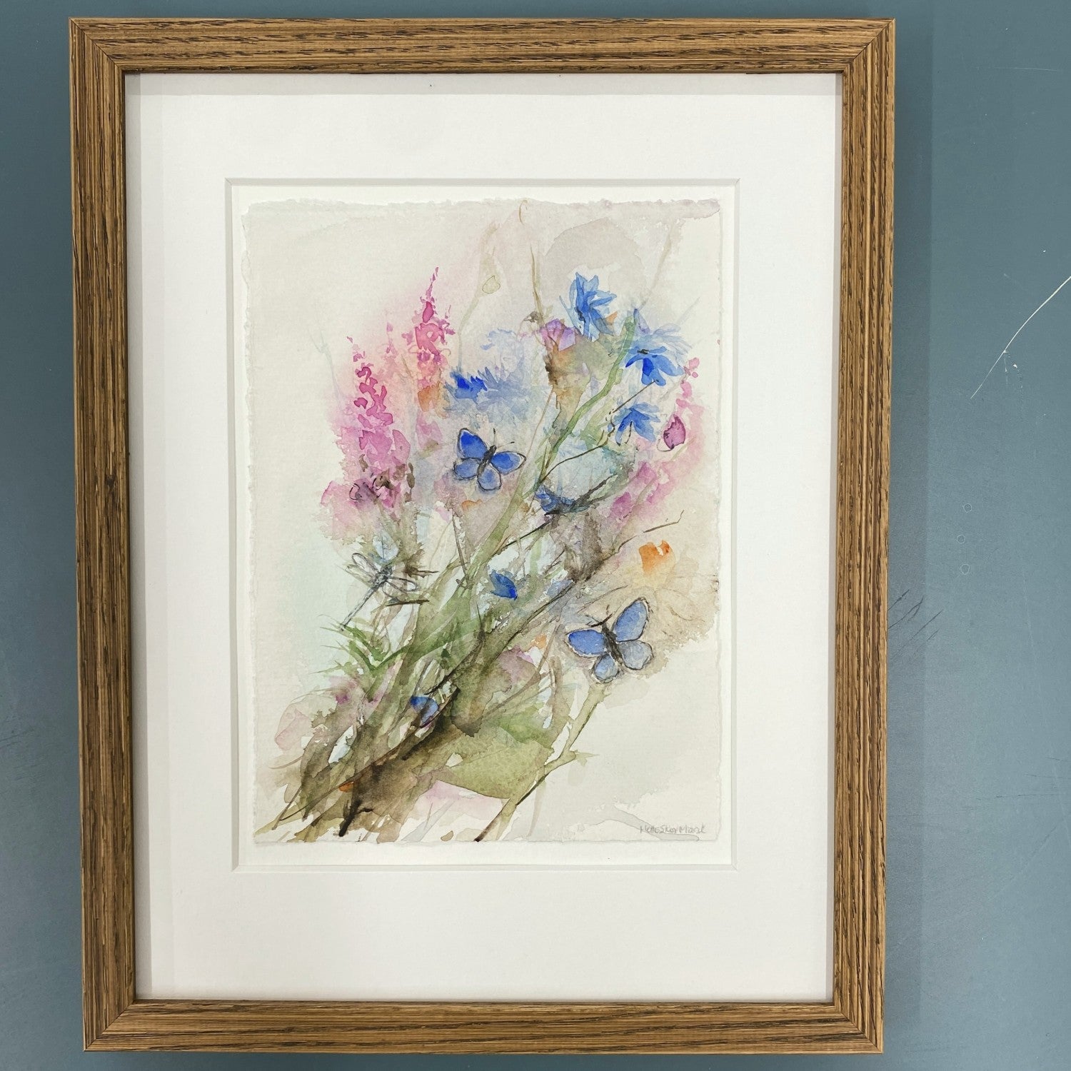Akvarel med blomster gederams og kornblomst, lyserød og blå farver. samt to blå sommerfugle og en guldsmed. indrammet i mørk eg.